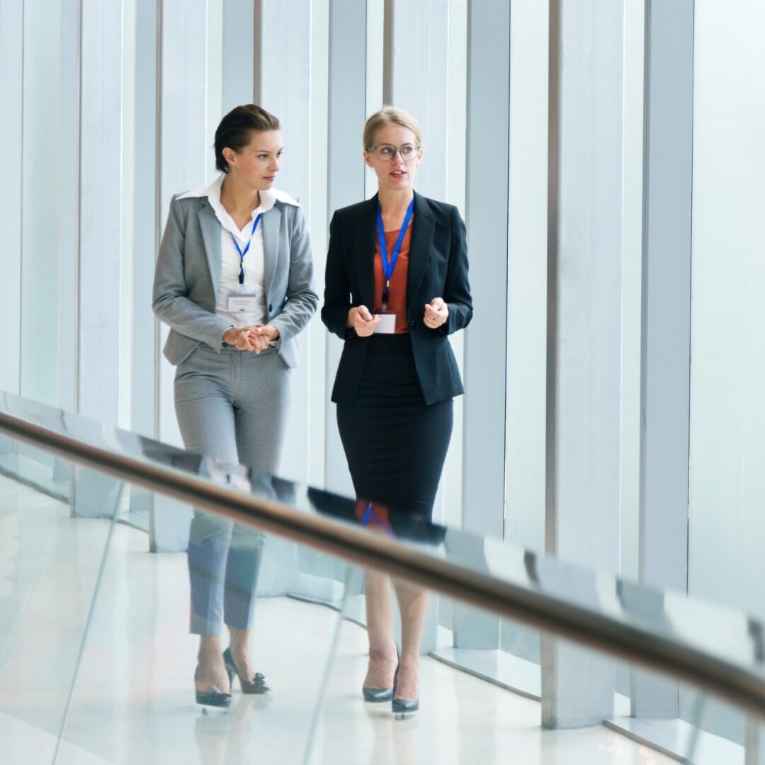 Twee zakenvrouwen overleggen al lopend over de gang.
